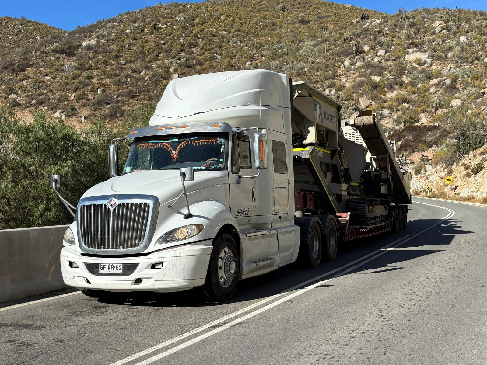 Camión blanco International de Transportes JSV trasladando maquinaria por carretera